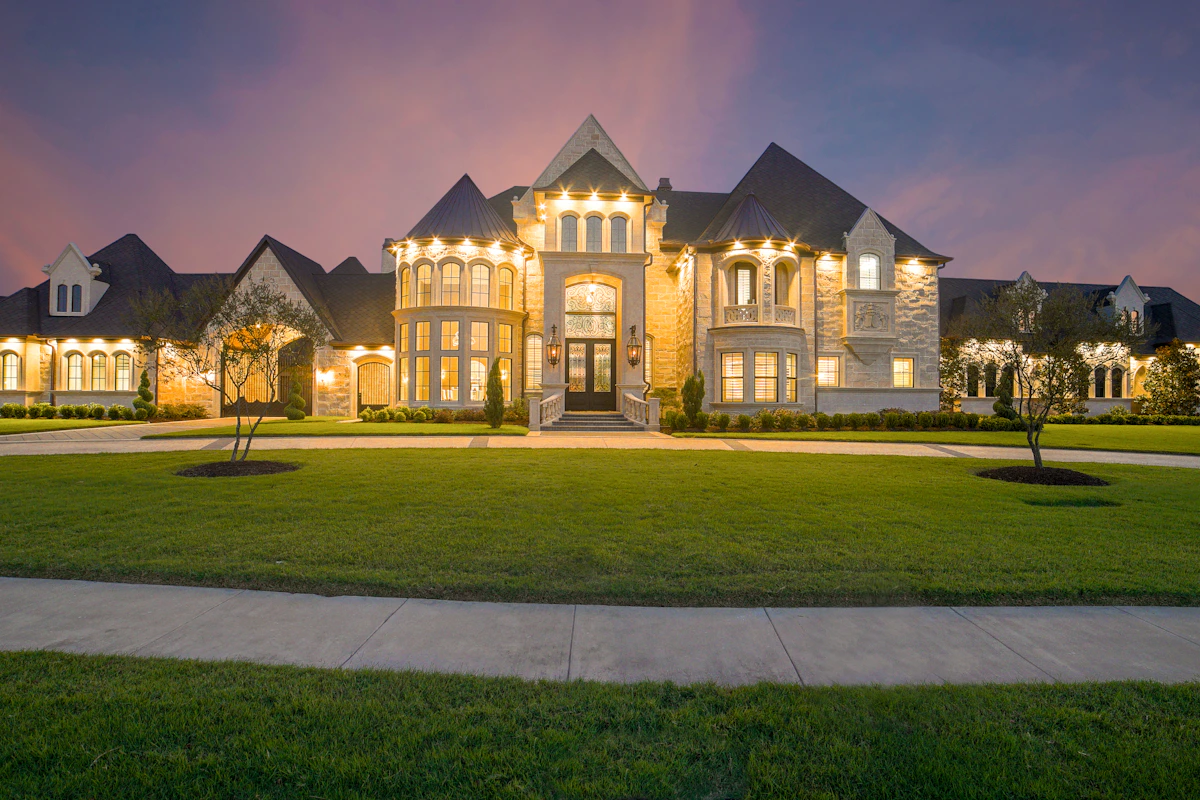 Multi-million dollar custom stone estate residence illuminated at dusk with expansive grounds
